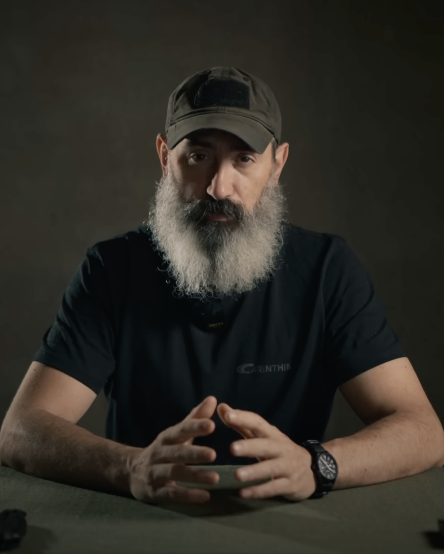 Man with a beard and cap sitting at a table against a dark background