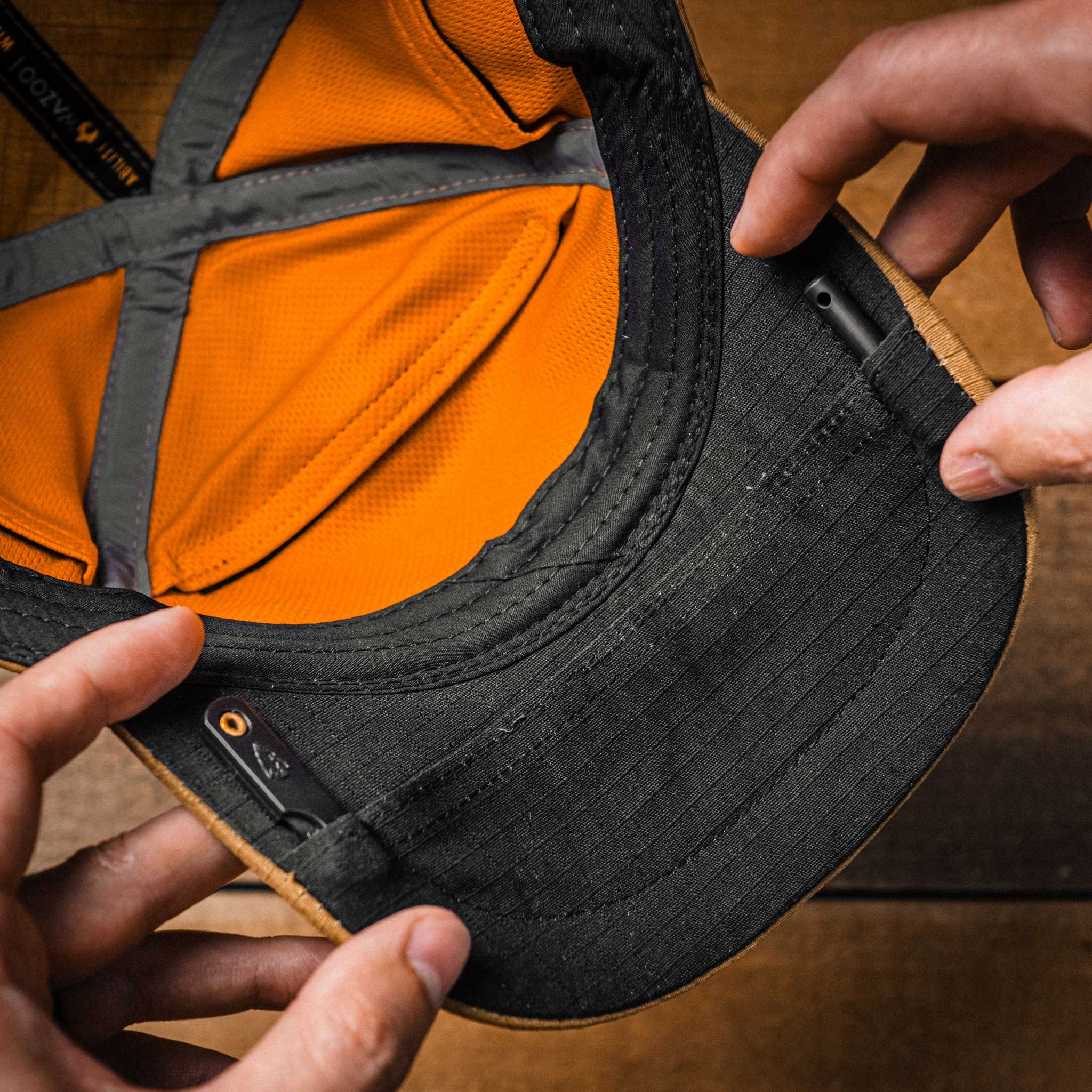 Close-up of a black cap with hands putting items into pockets on the brim of the hat.