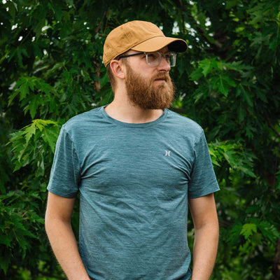 Man wearing a blue t-shirt with a logo and a tan cap outdoors