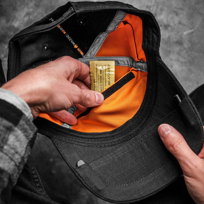 A man pulling water purification tablets out of a pocket in the underside of a black hat