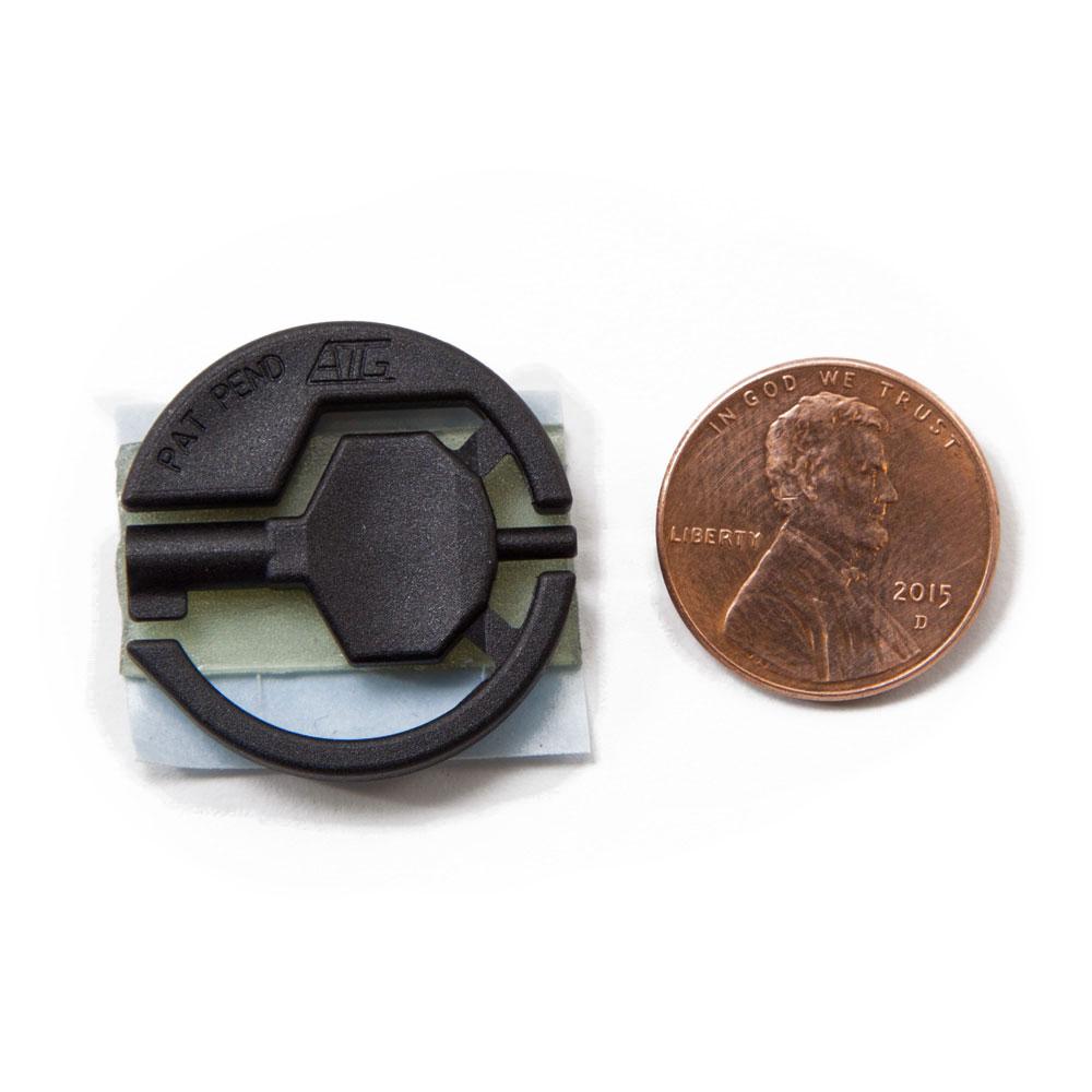 Black handcuff key with adhesive backing attached laid flat next to a penny for size comparison